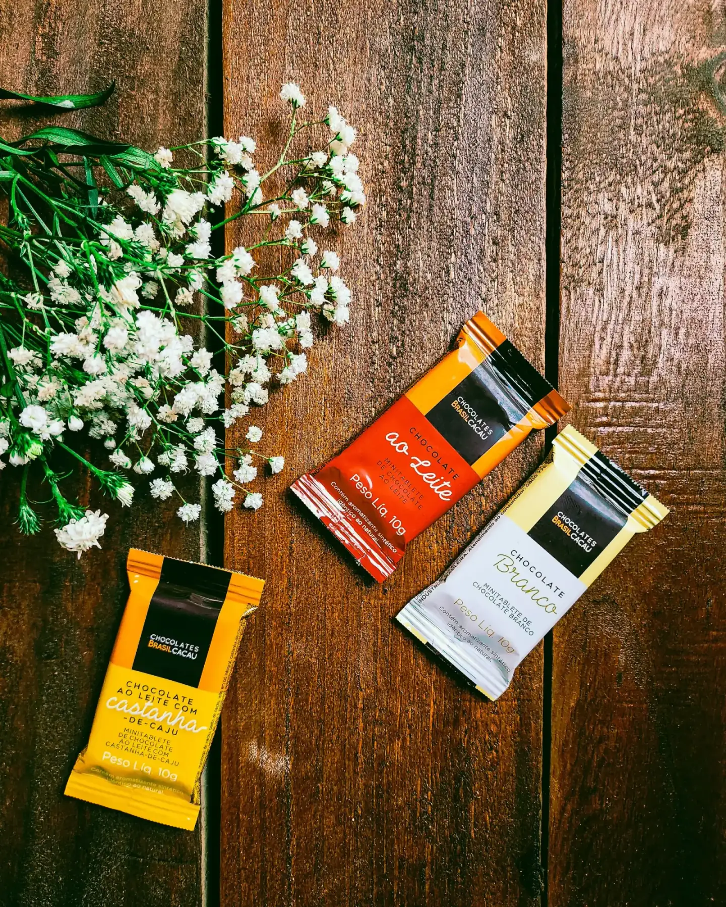 Three chocolate bar wrappers on a wooden table with flowers