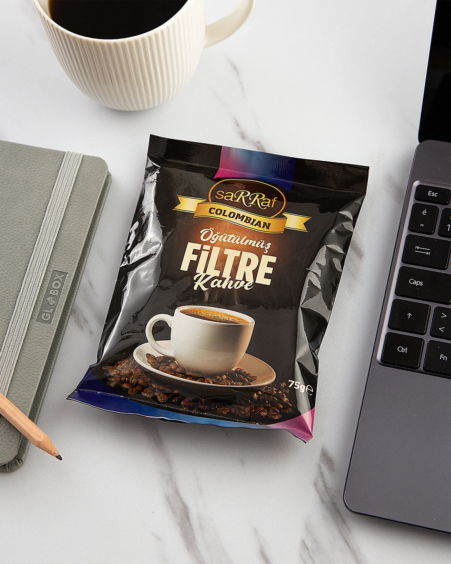 Printed coffee pouch on a marble desk with a cup and laptop