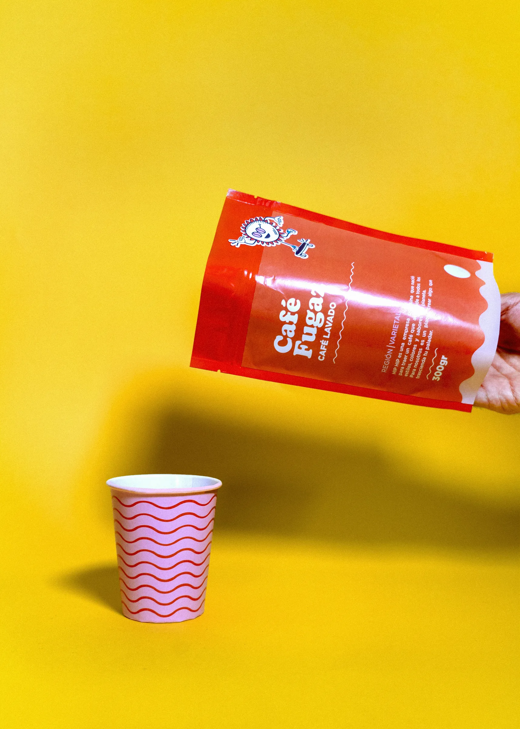 Red printed coffee pouch and a striped paper cup on yellow