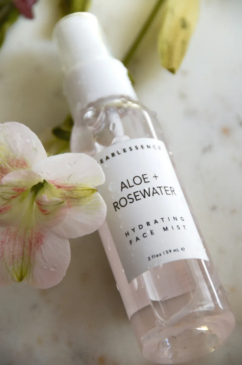 Clear spray bottle of face mist with a white printed label beside flowers