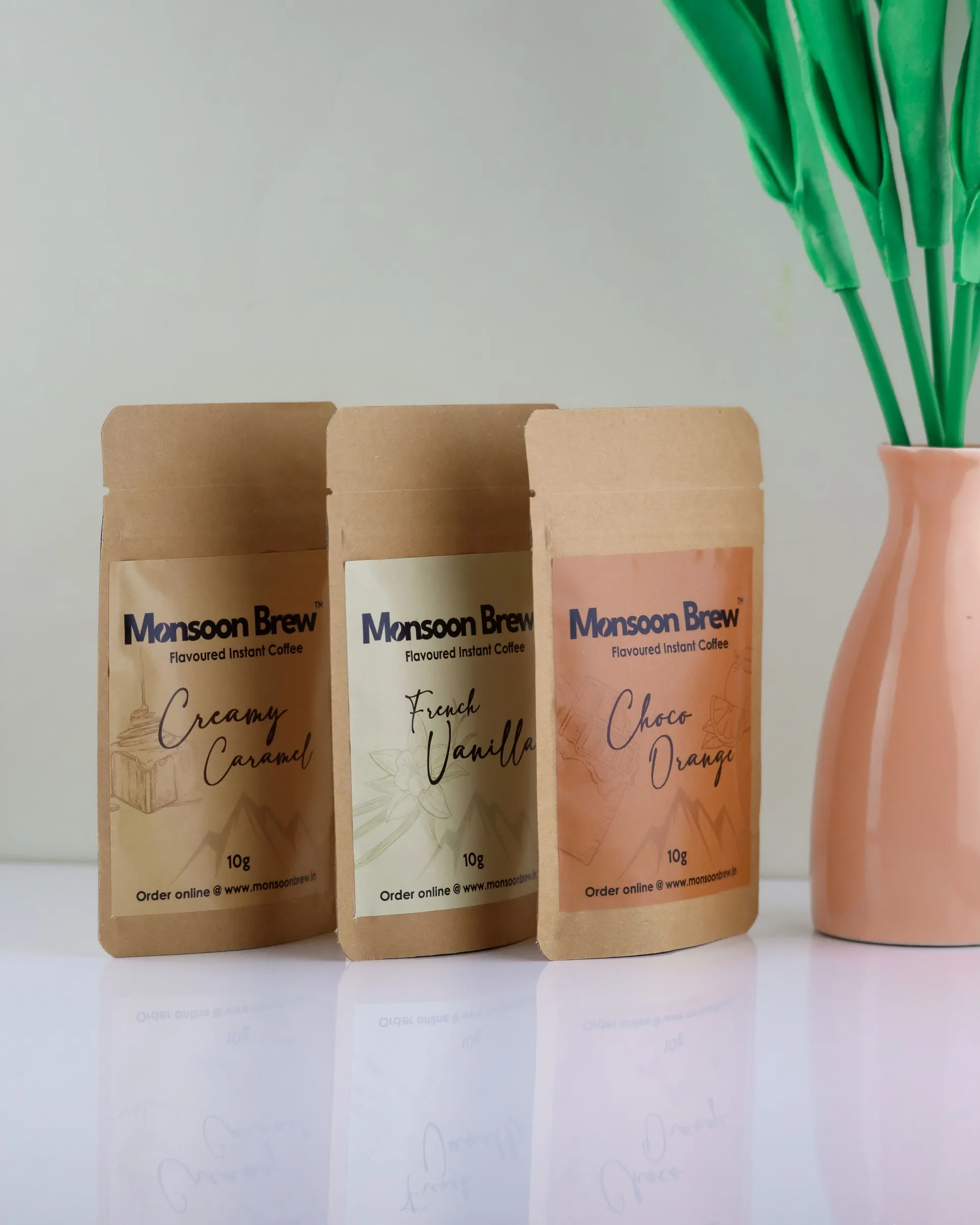 Three kraft paper coffee sachets with printed flavour labels beside a pink vase