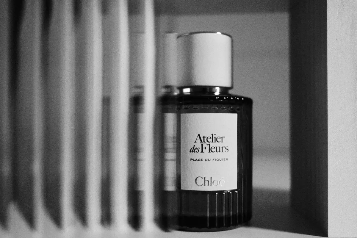 Black and white photo of a glass perfume bottle with a printed label on a shelf