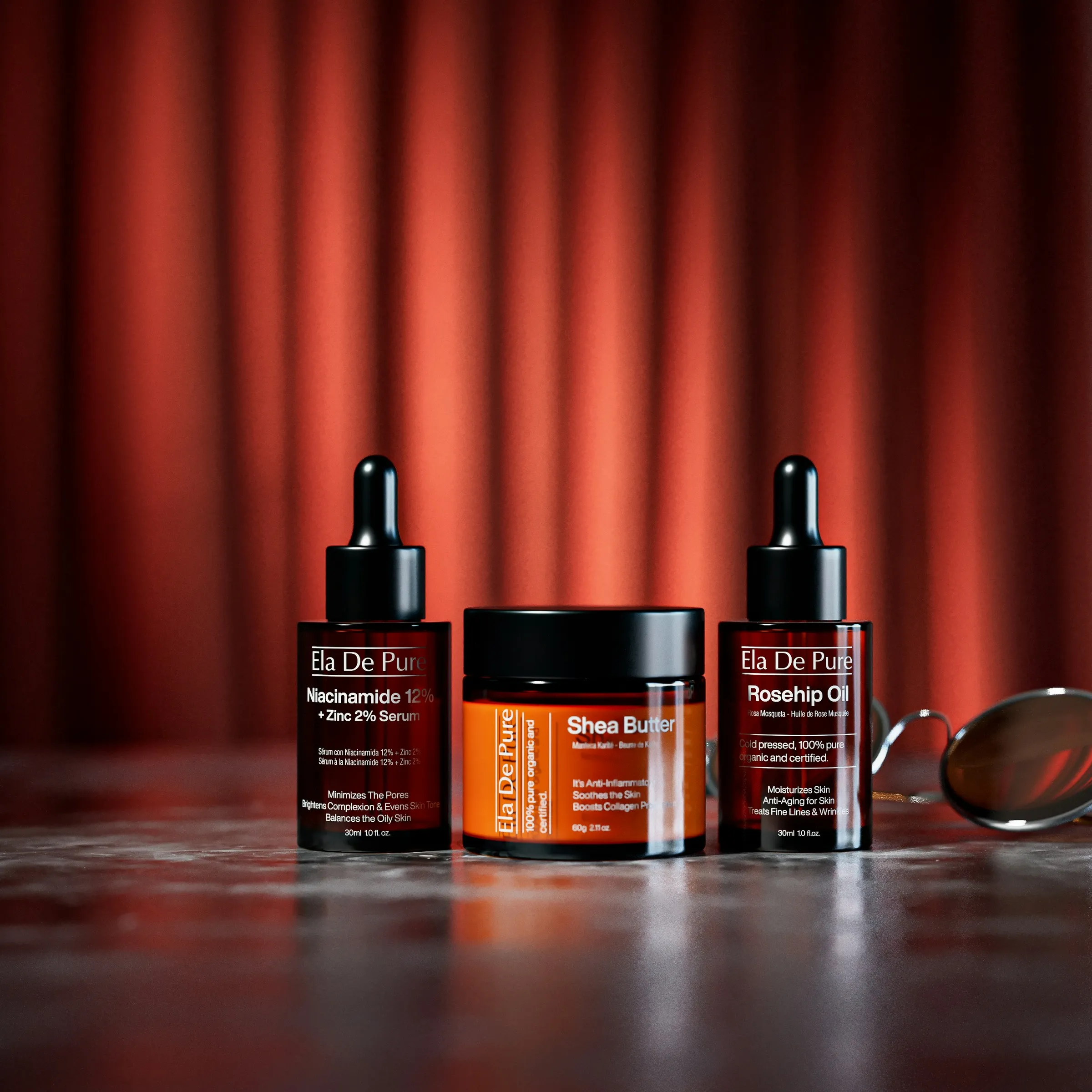 Two amber dropper bottles and a jar with orange labels in front of a red curtain