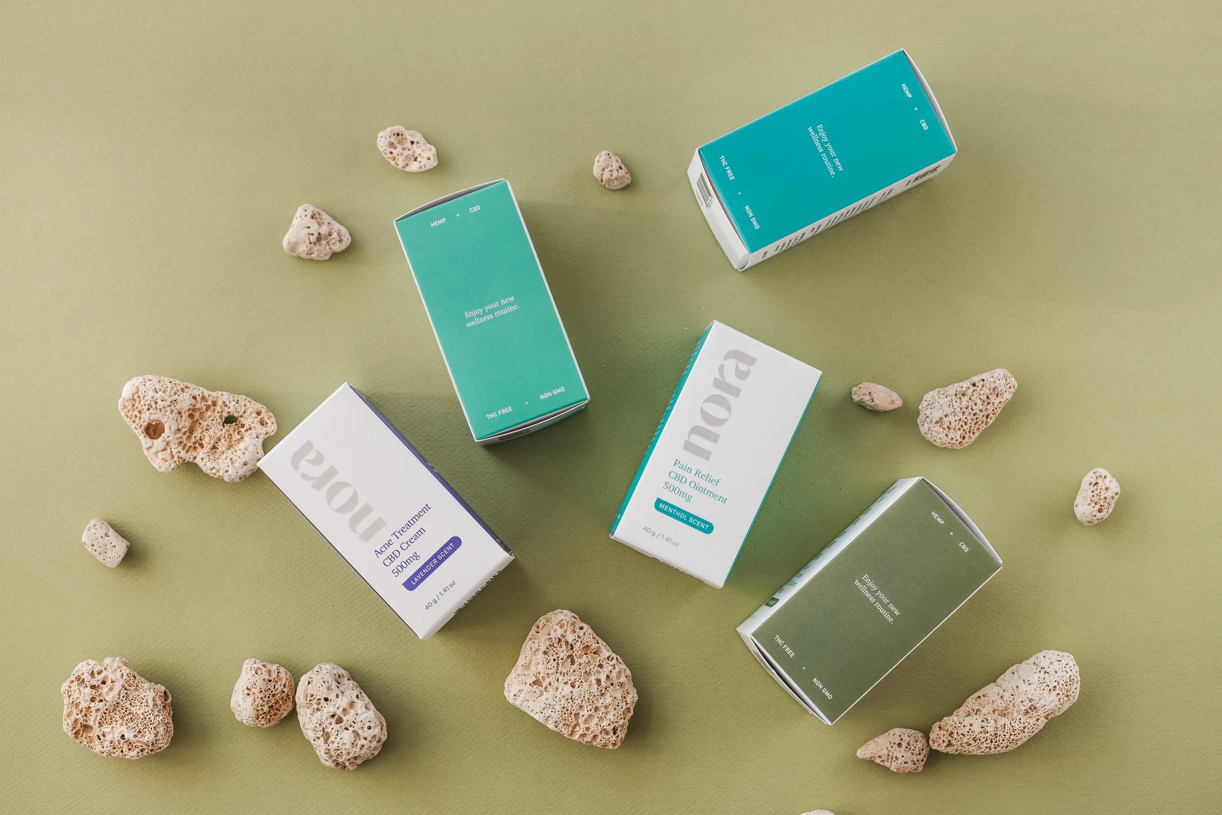 Teal and white skincare cartons with pumice stones on green