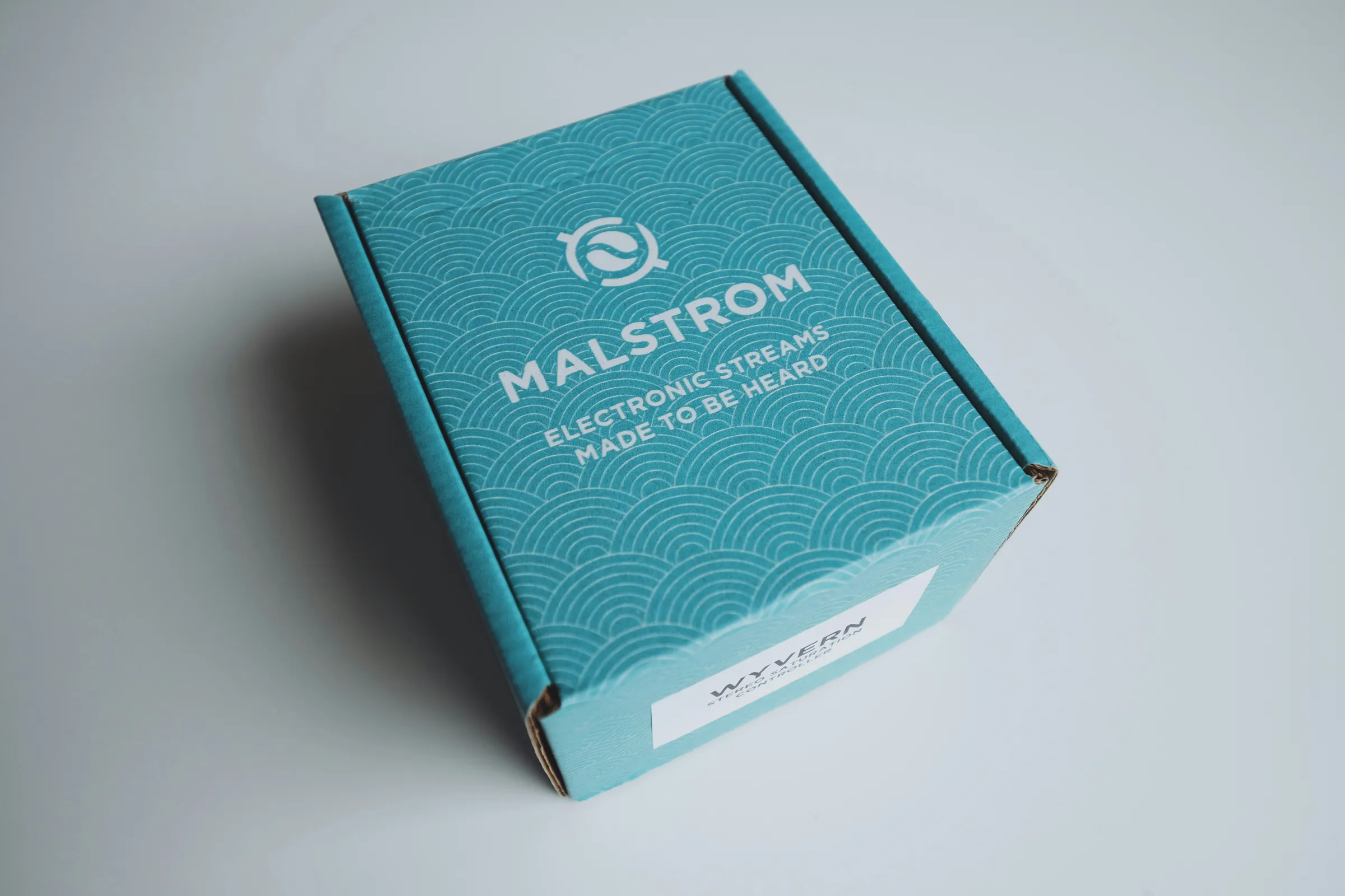 Teal printed mailer box with a wave pattern and a white address label
