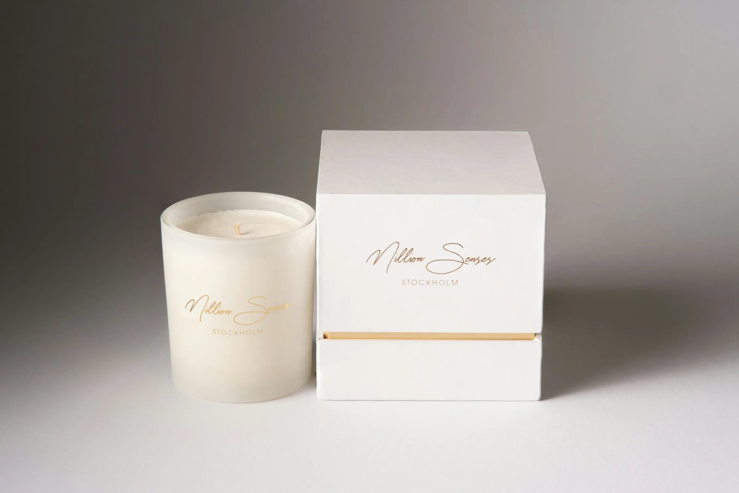White candle in glass beside a white rigid lid and base box with gold foil script